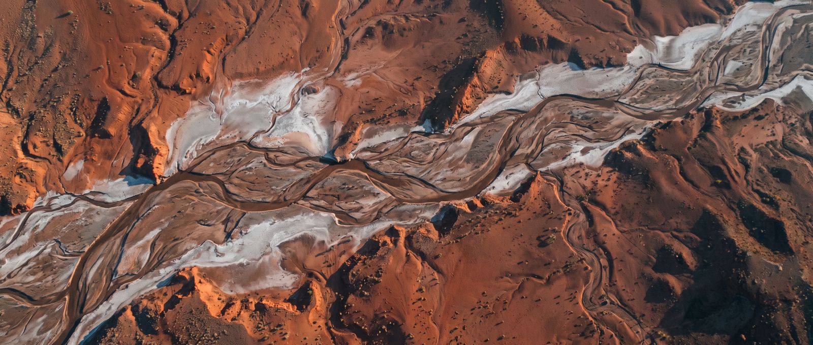 Red earth and pale braided river channels seen from high altitude in morning light