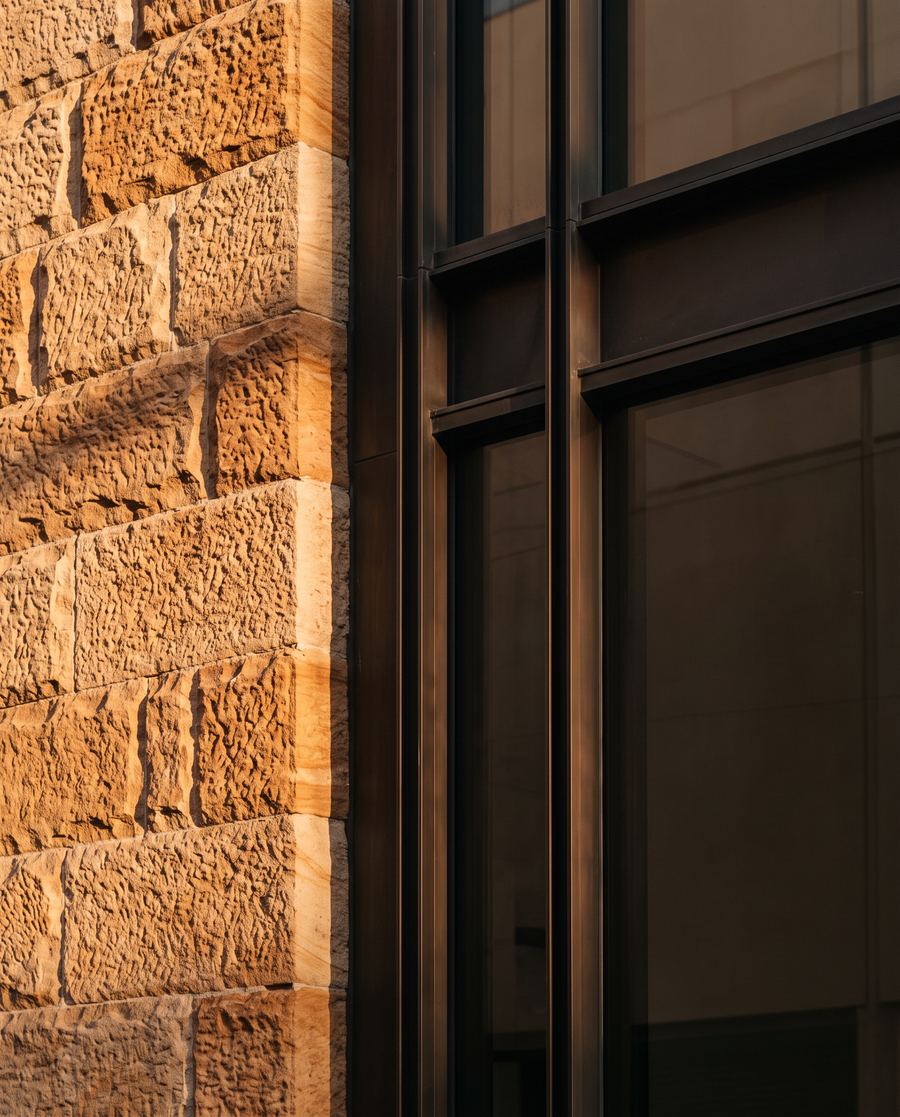Late sun across a sandstone wall beside a bronze and glass facade
